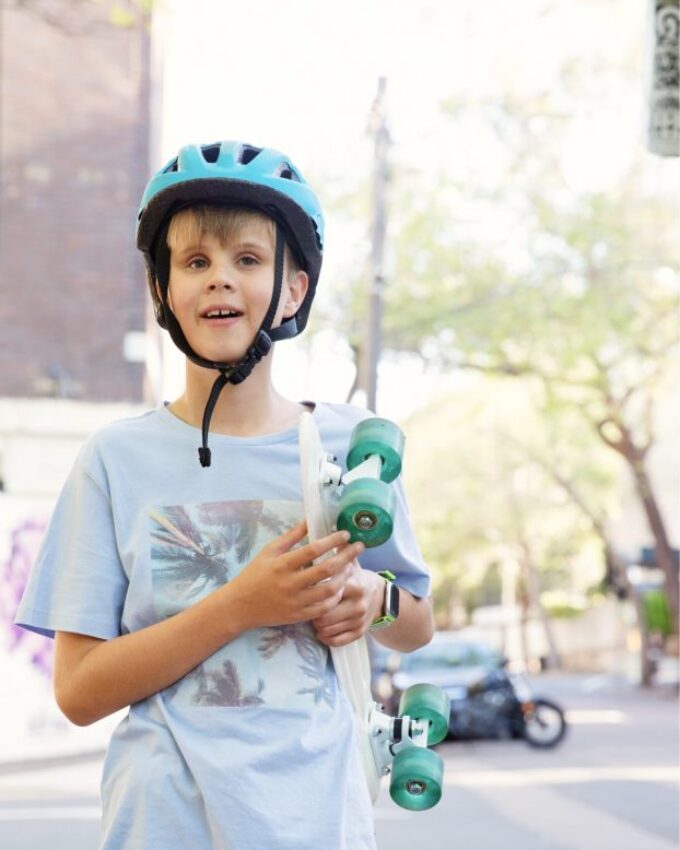Young boy with helmet on holding a skateboard smiles at camera.